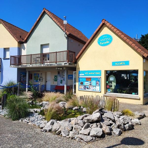 Batiment du camping avec jardin et panneaux d'accueil.