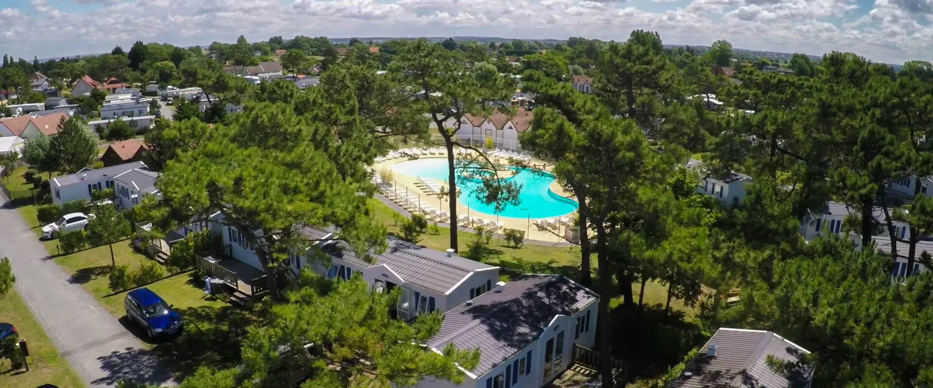 Vue aérienne d'un camping avec piscine et chalets.