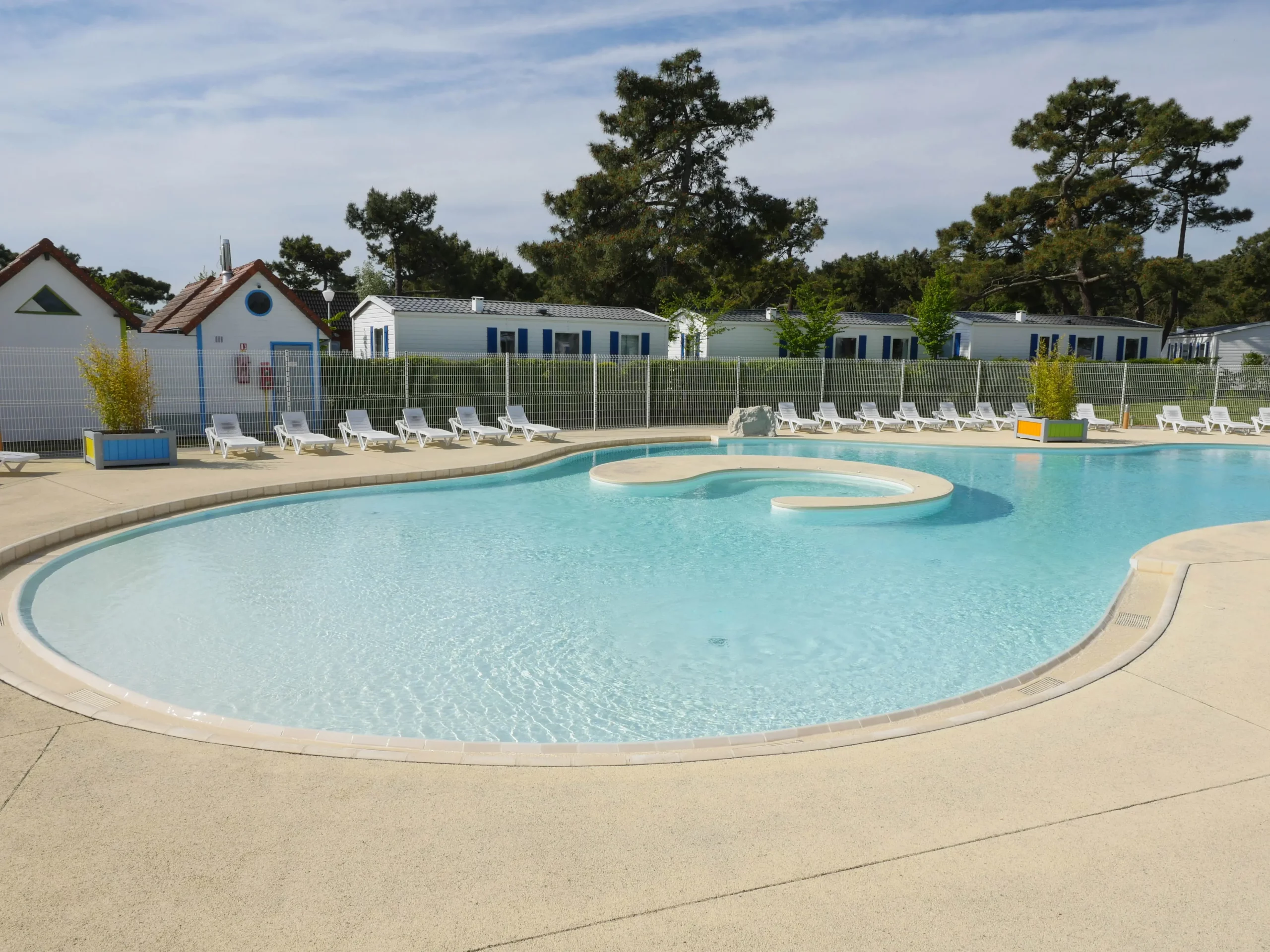 Piscine entourée de transats et maisons de vacances.