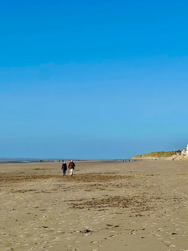 Deux personnes marchent sur une plage ensoleillée.