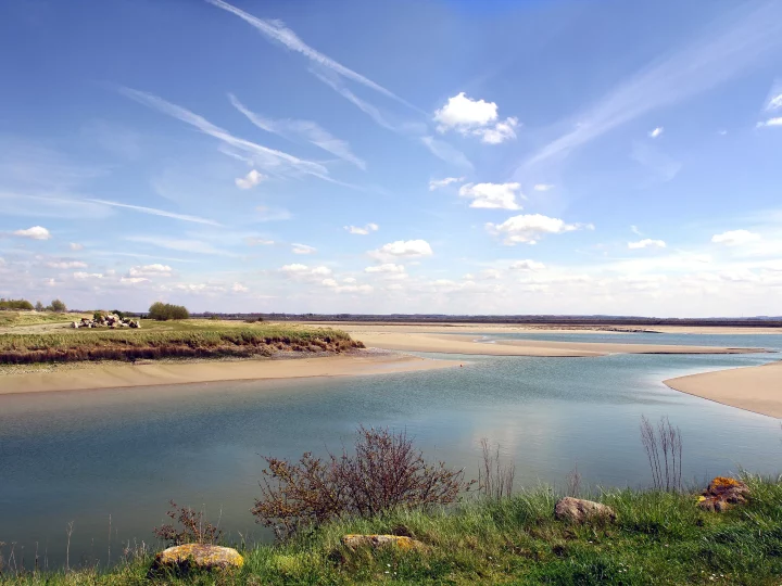 Vue d'une rivière avec nuages et verdure.