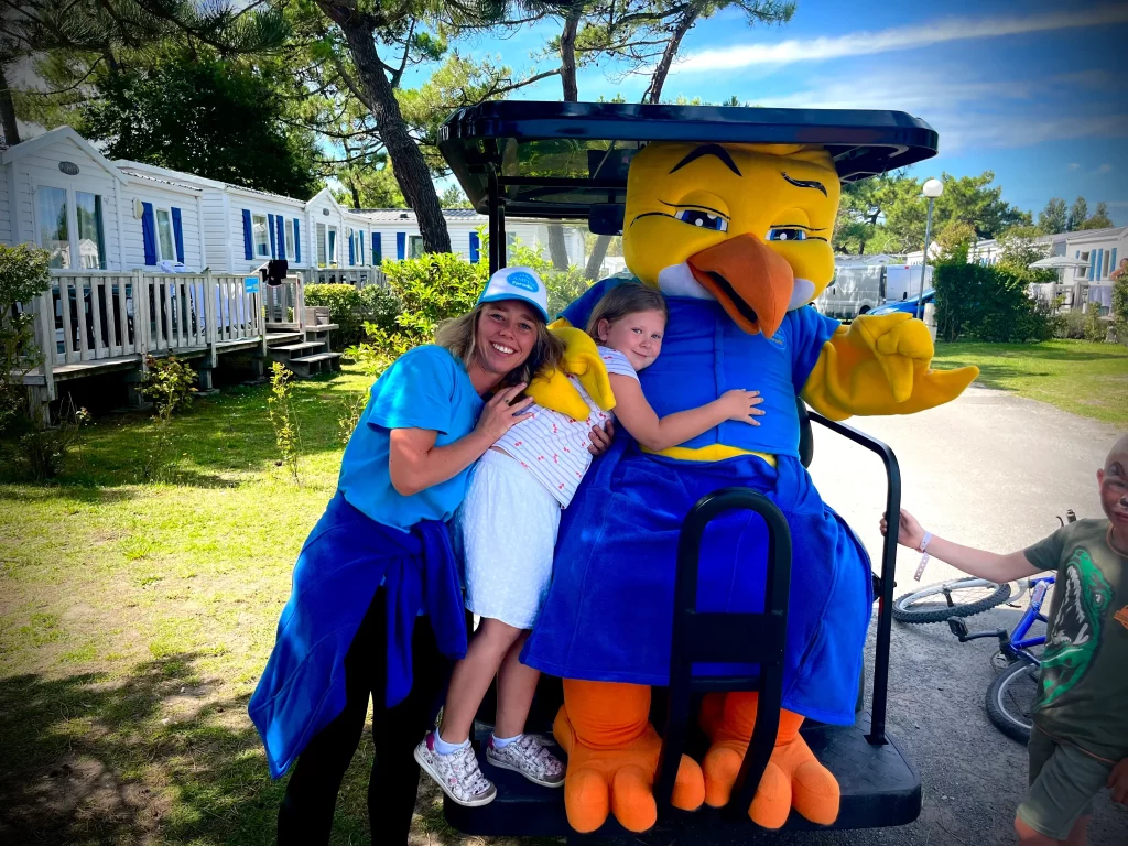 Enfant avec mascotte et adultes souriants à l'extérieur.