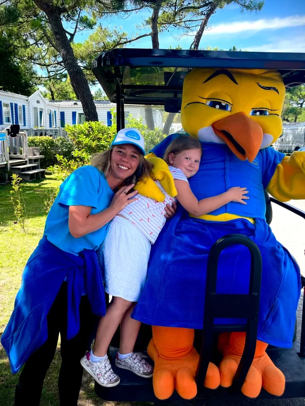 Enfant avec mascotte et adultes souriants à l'extérieur.