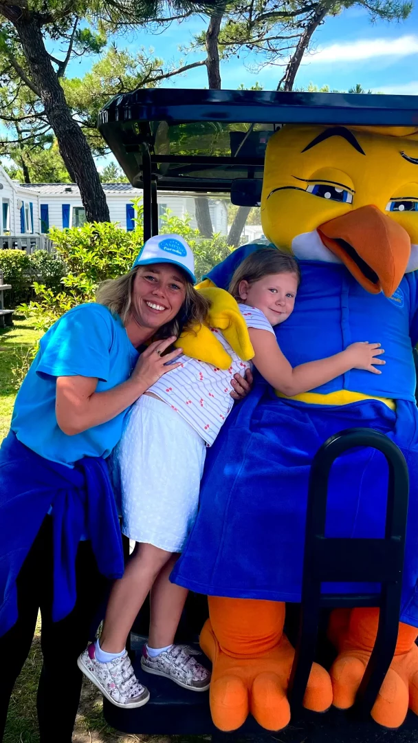 Enfant avec mascotte et adultes souriants à l'extérieur.