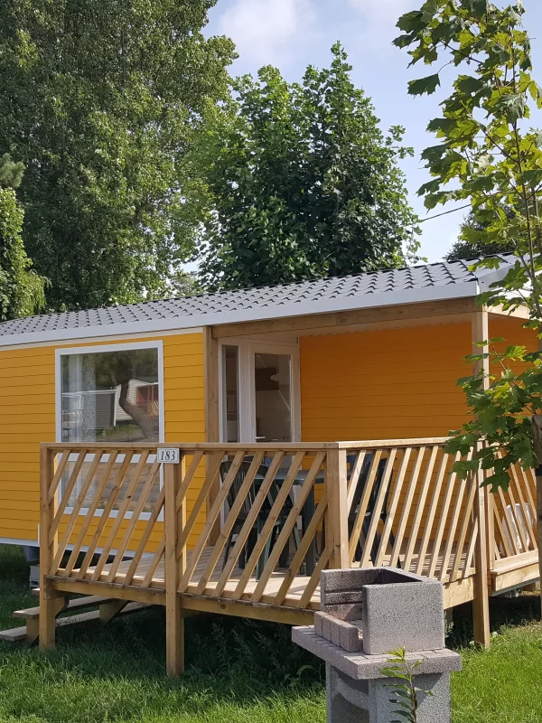 Mobil-home jaune avec terrasse et arbres environnants.