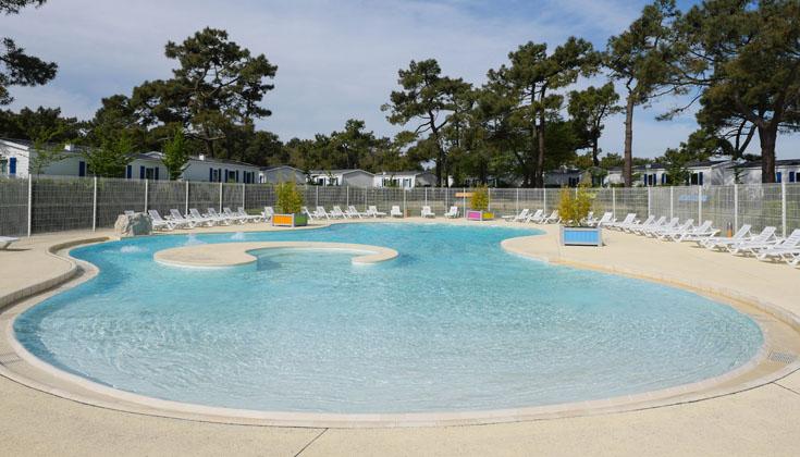 Piscine entourée de transats et de verdure.