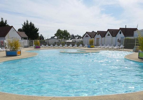 Piscine et cabanes dans un camping ensoleillé.