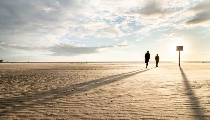 Deux personnes marchant sur une plage ensoleillée.