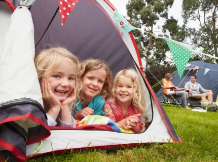 Trois enfants souriants dans une tente de camping.